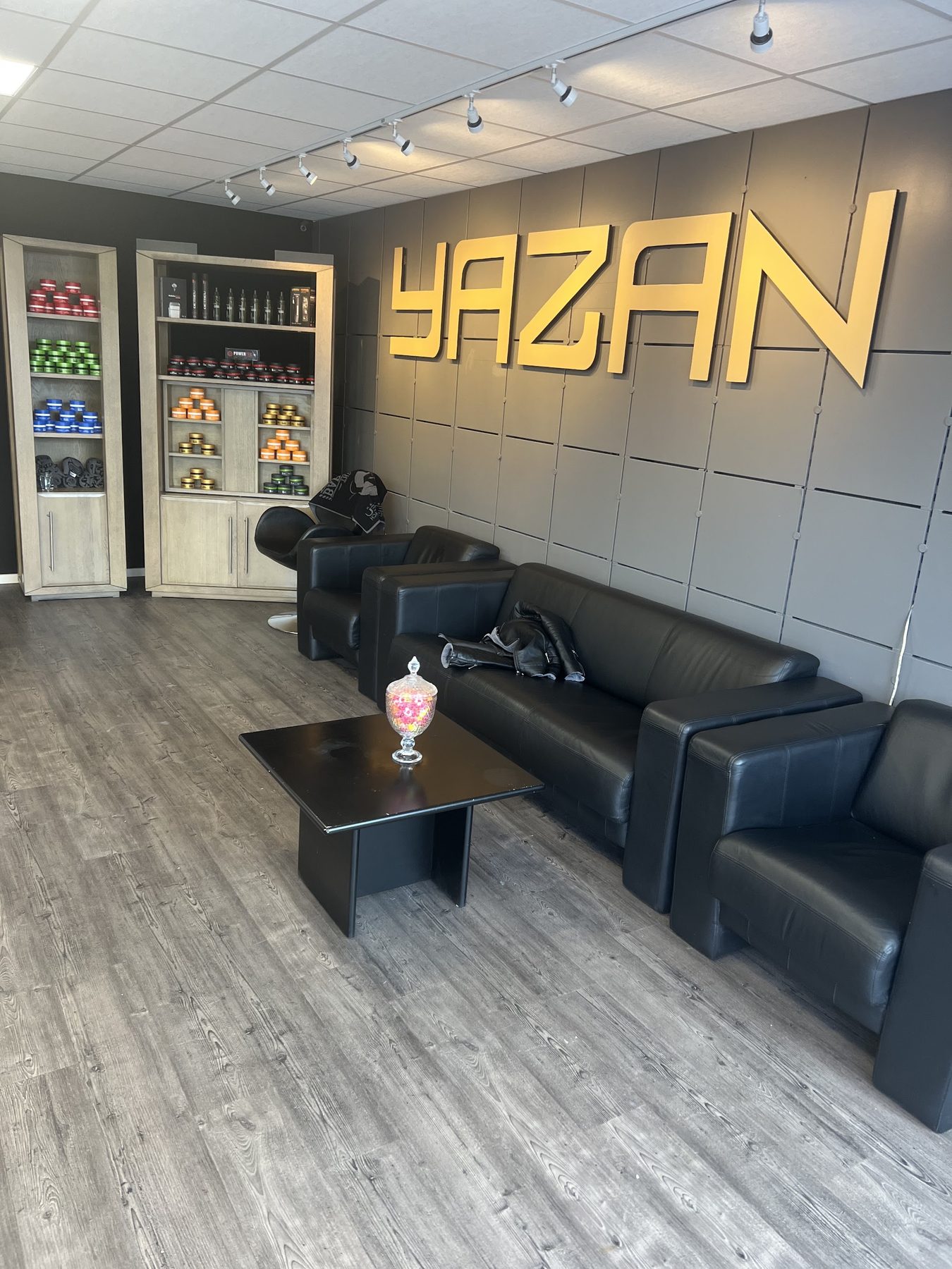 Zithoek met zwarte leren banken en de gouden letters YAZAN aan de wand